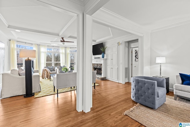 living room with coffered ceiling, ornamental molding, a fireplace, and light hardwood / wood-style flooring