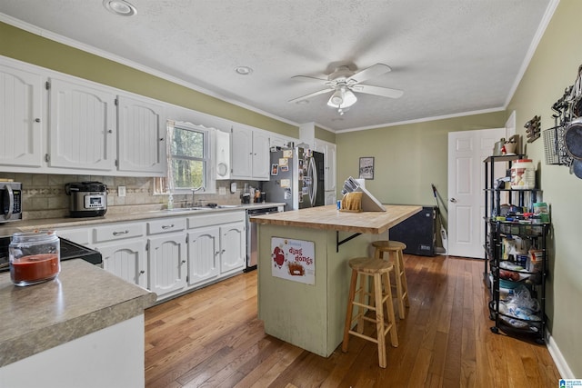 kitchen with sink, light hardwood / wood-style flooring, appliances with stainless steel finishes, a kitchen island, and white cabinets