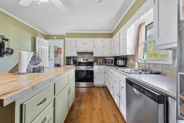 kitchen with appliances with stainless steel finishes, sink, white cabinets, ornamental molding, and light hardwood / wood-style flooring