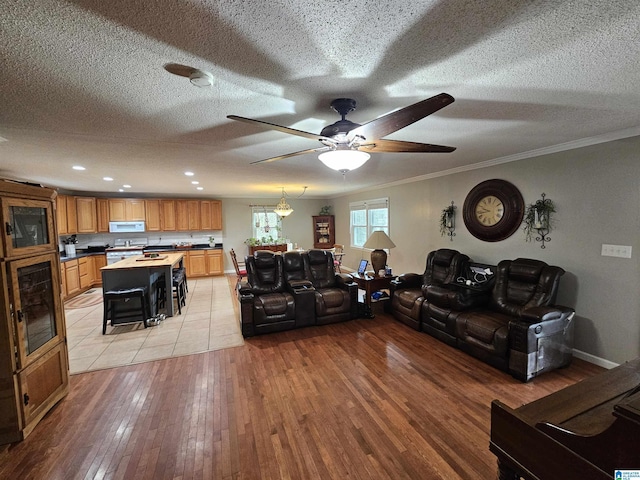 living room featuring ornamental molding, ceiling fan, a textured ceiling, and light hardwood / wood-style flooring