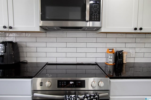 kitchen with stainless steel appliances, tasteful backsplash, white cabinets, and dark stone counters