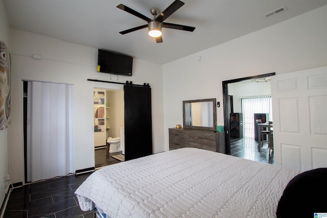 bedroom with ceiling fan, a barn door, and dark tile patterned floors