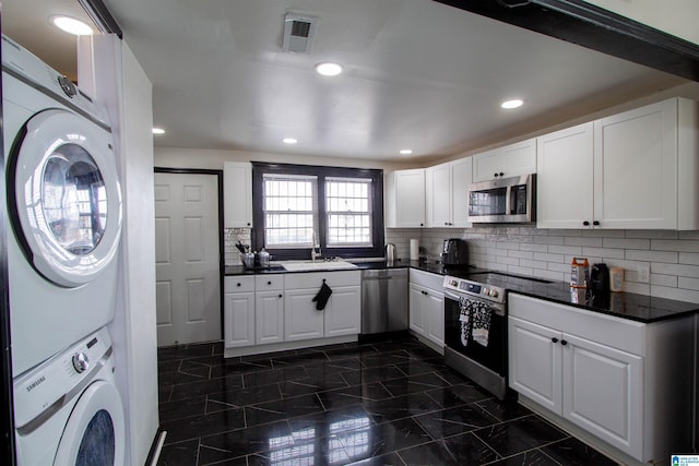 kitchen featuring sink, white cabinetry, backsplash, stainless steel appliances, and stacked washer / dryer