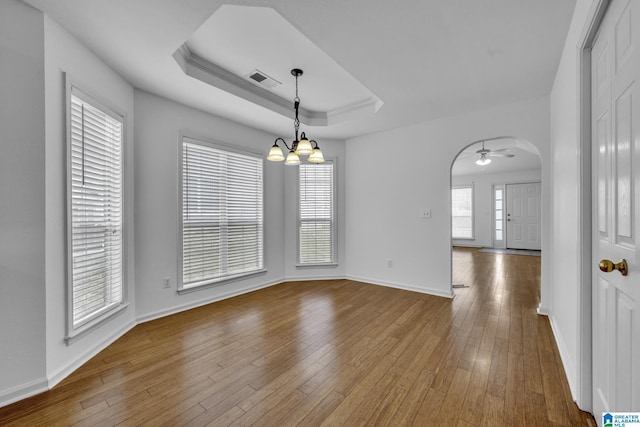 empty room with a raised ceiling, hardwood / wood-style flooring, and ceiling fan with notable chandelier