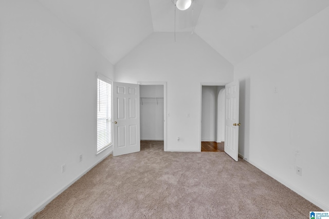 unfurnished bedroom featuring ceiling fan, a spacious closet, high vaulted ceiling, and light carpet