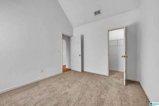 unfurnished bedroom with a walk in closet, light colored carpet, high vaulted ceiling, and a closet