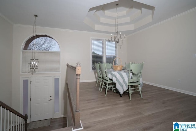 dining space featuring wood-type flooring, ornamental molding, an inviting chandelier, and a tray ceiling