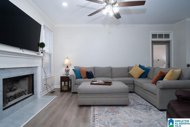 living room with crown molding, ceiling fan, a fireplace, and light hardwood / wood-style flooring