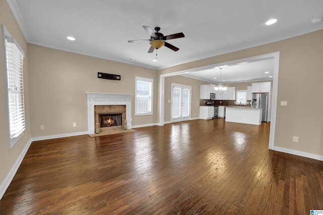 unfurnished living room featuring a tiled fireplace, crown molding, dark wood-type flooring, and ceiling fan with notable chandelier