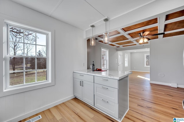 kitchen with decorative light fixtures, coffered ceiling, kitchen peninsula, light stone countertops, and light hardwood / wood-style flooring