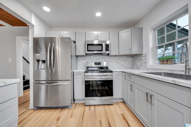 kitchen featuring tasteful backsplash, appliances with stainless steel finishes, sink, and light hardwood / wood-style flooring