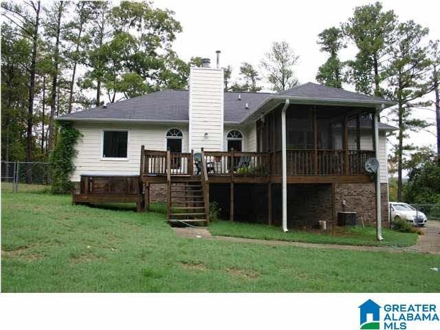 rear view of house with a chimney, a lawn, a sunroom, a wooden deck, and stairs