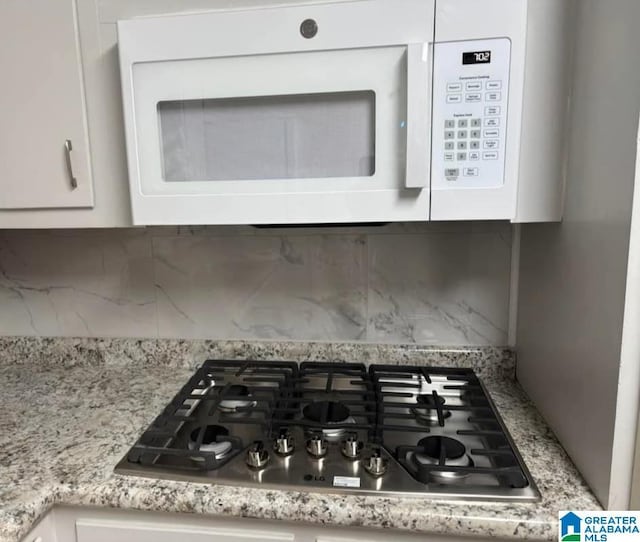 details with tasteful backsplash, stainless steel gas stovetop, light stone counters, and white cabinets