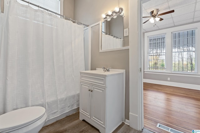 bathroom with toilet, vanity, ceiling fan, hardwood / wood-style floors, and a drop ceiling