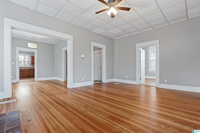 unfurnished living room with a drop ceiling, ceiling fan, and light hardwood / wood-style flooring