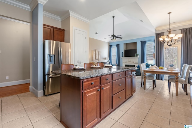 kitchen with light tile patterned flooring, pendant lighting, dark stone countertops, stainless steel fridge, and a center island