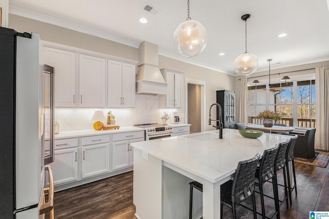 kitchen with high quality range, a kitchen island with sink, white cabinetry, custom exhaust hood, and freestanding refrigerator