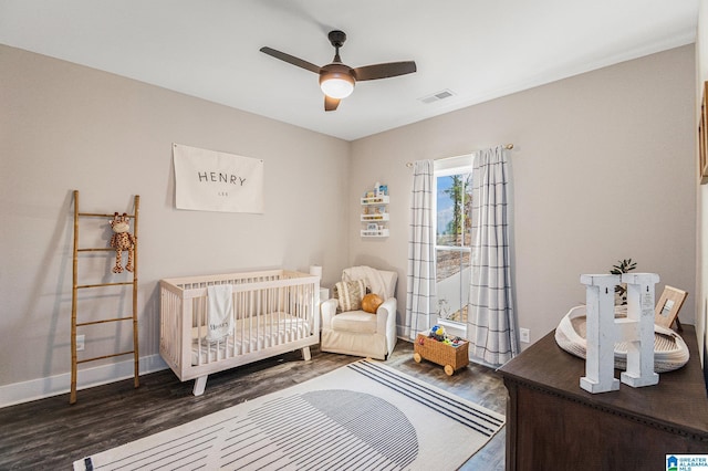 bedroom with a crib, baseboards, visible vents, a ceiling fan, and dark wood-type flooring