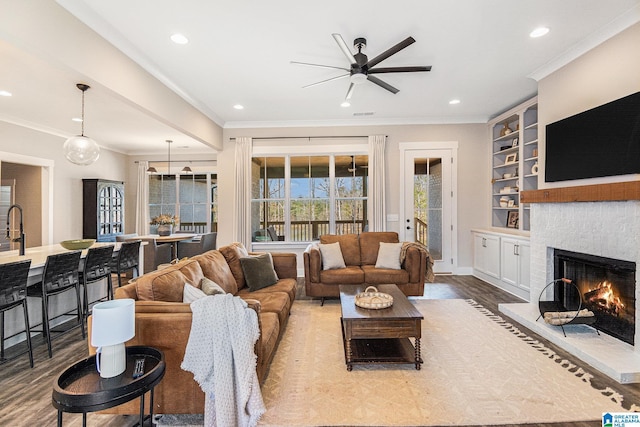 living area with a warm lit fireplace, ornamental molding, light wood-style flooring, and recessed lighting