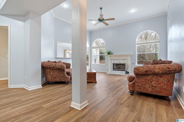 living room featuring a premium fireplace, ornamental molding, ceiling fan, and light wood-type flooring