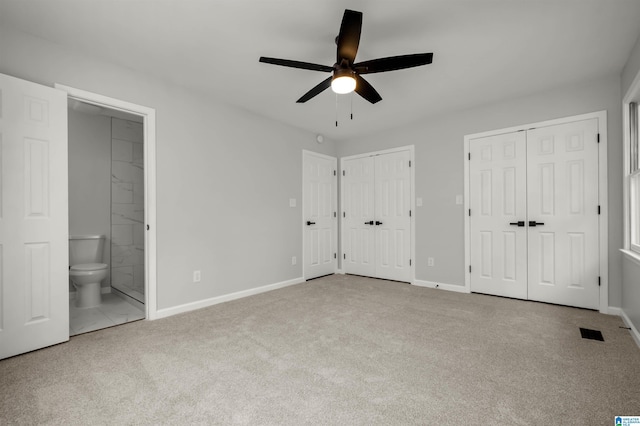 unfurnished bedroom featuring two closets, ensuite bath, light colored carpet, and ceiling fan