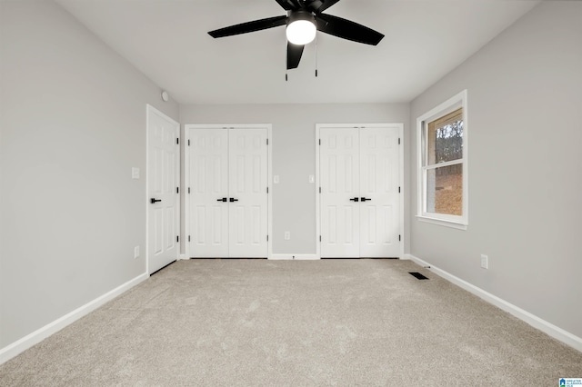 unfurnished bedroom featuring multiple closets, ceiling fan, and light carpet