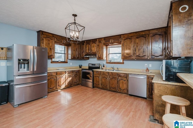 kitchen with sink, hanging light fixtures, stainless steel appliances, light hardwood / wood-style floors, and a textured ceiling