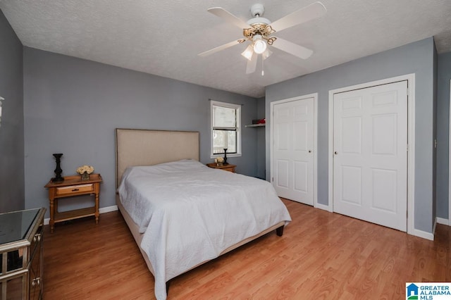 bedroom featuring ceiling fan, hardwood / wood-style flooring, a textured ceiling, and multiple closets