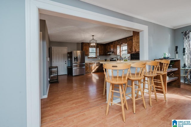 kitchen with ornamental molding, kitchen peninsula, light wood-type flooring, and stainless steel fridge with ice dispenser