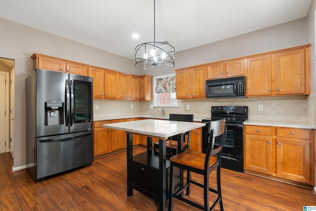 kitchen with light stone countertops, pendant lighting, dark hardwood / wood-style flooring, and black appliances