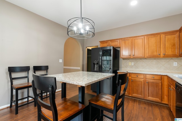 kitchen with light stone counters, hanging light fixtures, dark hardwood / wood-style flooring, decorative backsplash, and black appliances