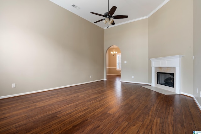 unfurnished living room with crown molding, a tile fireplace, ceiling fan, a towering ceiling, and dark hardwood / wood-style flooring