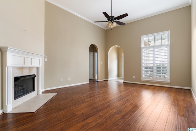 unfurnished living room featuring a tiled fireplace, ornamental molding, a high ceiling, ceiling fan, and light hardwood / wood-style floors