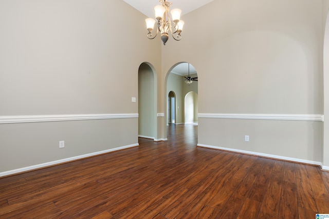 empty room with dark hardwood / wood-style floors, ceiling fan with notable chandelier, and a high ceiling