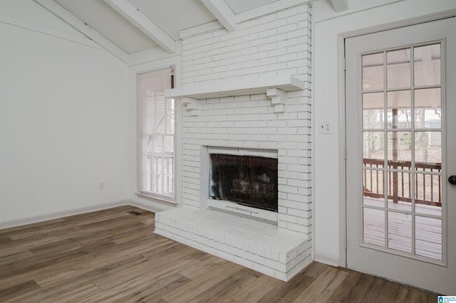 unfurnished living room with a healthy amount of sunlight, wood-type flooring, a fireplace, and vaulted ceiling with beams