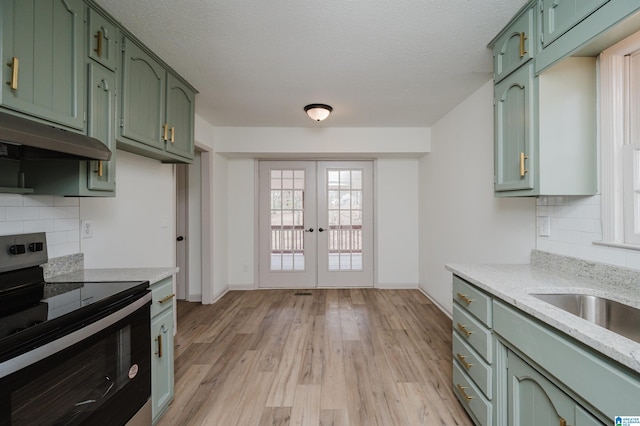 kitchen featuring stainless steel electric range oven, green cabinets, decorative backsplash, and light hardwood / wood-style flooring