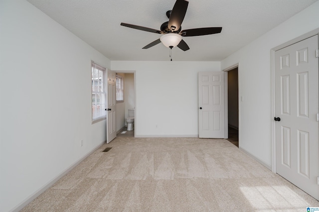 unfurnished bedroom featuring ceiling fan, ensuite bathroom, light carpet, and a textured ceiling