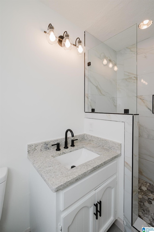 bathroom with vanity, a tile shower, a textured ceiling, and toilet