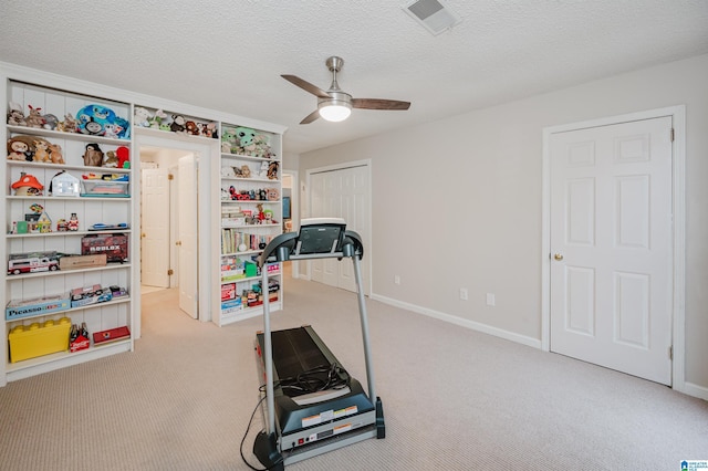 workout area featuring ceiling fan, light colored carpet, and a textured ceiling