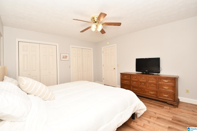 bedroom with two closets, light hardwood / wood-style floors, and ceiling fan