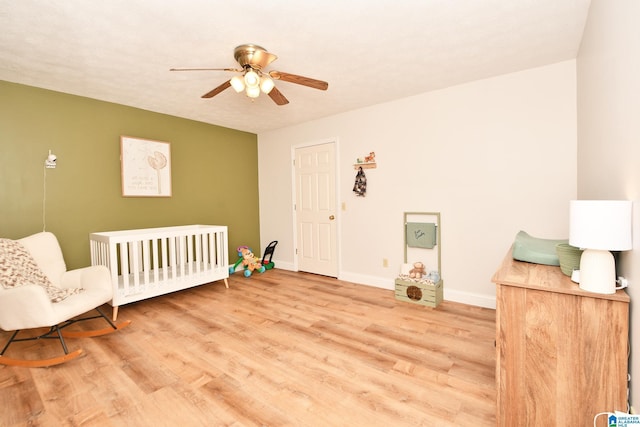 bedroom featuring a nursery area, ceiling fan, and light wood-type flooring