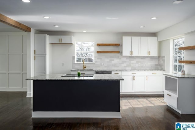 kitchen with a kitchen island, light stone countertops, a wealth of natural light, and white cabinets