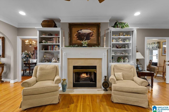 sitting room featuring a fireplace with flush hearth, a notable chandelier, ornamental molding, and wood finished floors