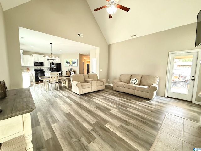 living room featuring ceiling fan with notable chandelier, light hardwood / wood-style flooring, and high vaulted ceiling