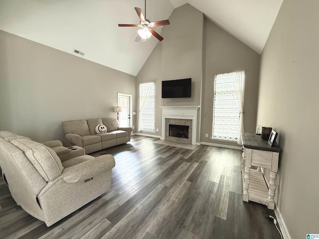 living room with dark wood-type flooring, ceiling fan, a tiled fireplace, and high vaulted ceiling