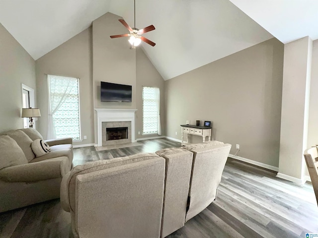 living room featuring a tiled fireplace, dark wood-type flooring, high vaulted ceiling, and ceiling fan