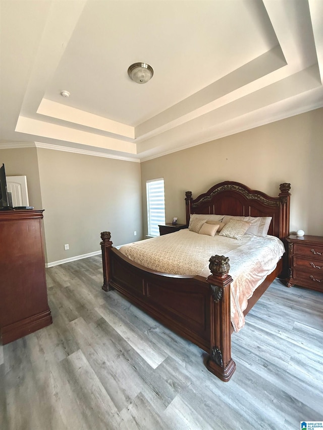 bedroom with hardwood / wood-style floors, ornamental molding, and a raised ceiling