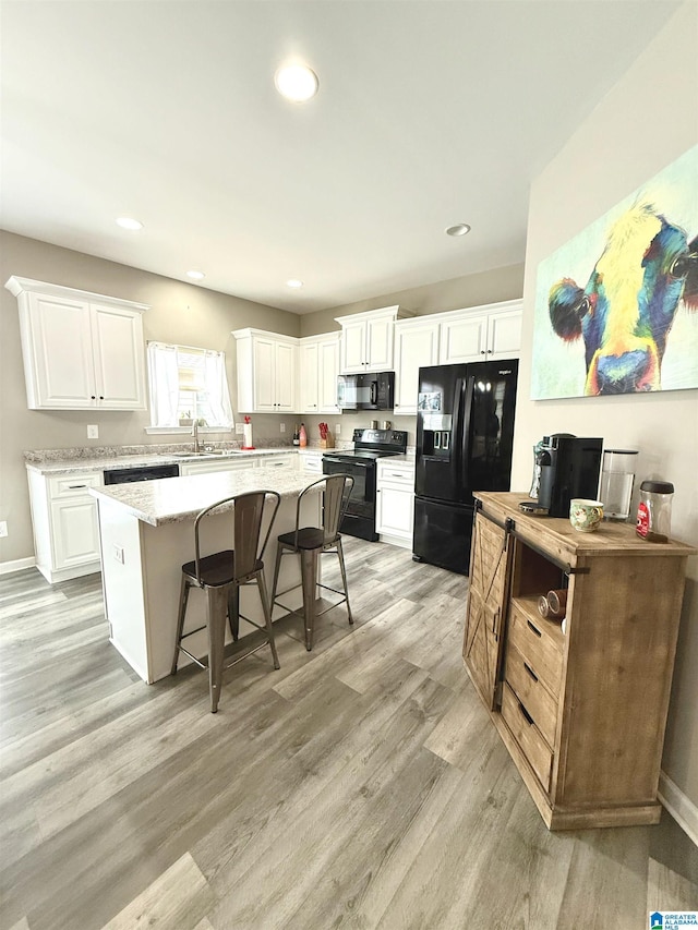 kitchen featuring white cabinetry, a center island, light stone countertops, and black appliances