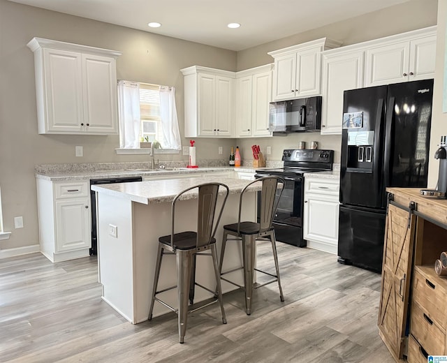 kitchen featuring a kitchen island, white cabinetry, sink, a kitchen bar, and black appliances