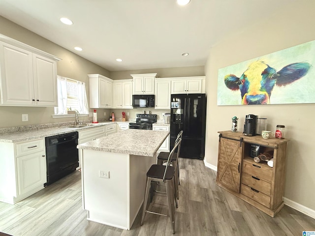 kitchen with white cabinetry, a kitchen bar, a center island, light hardwood / wood-style floors, and black appliances